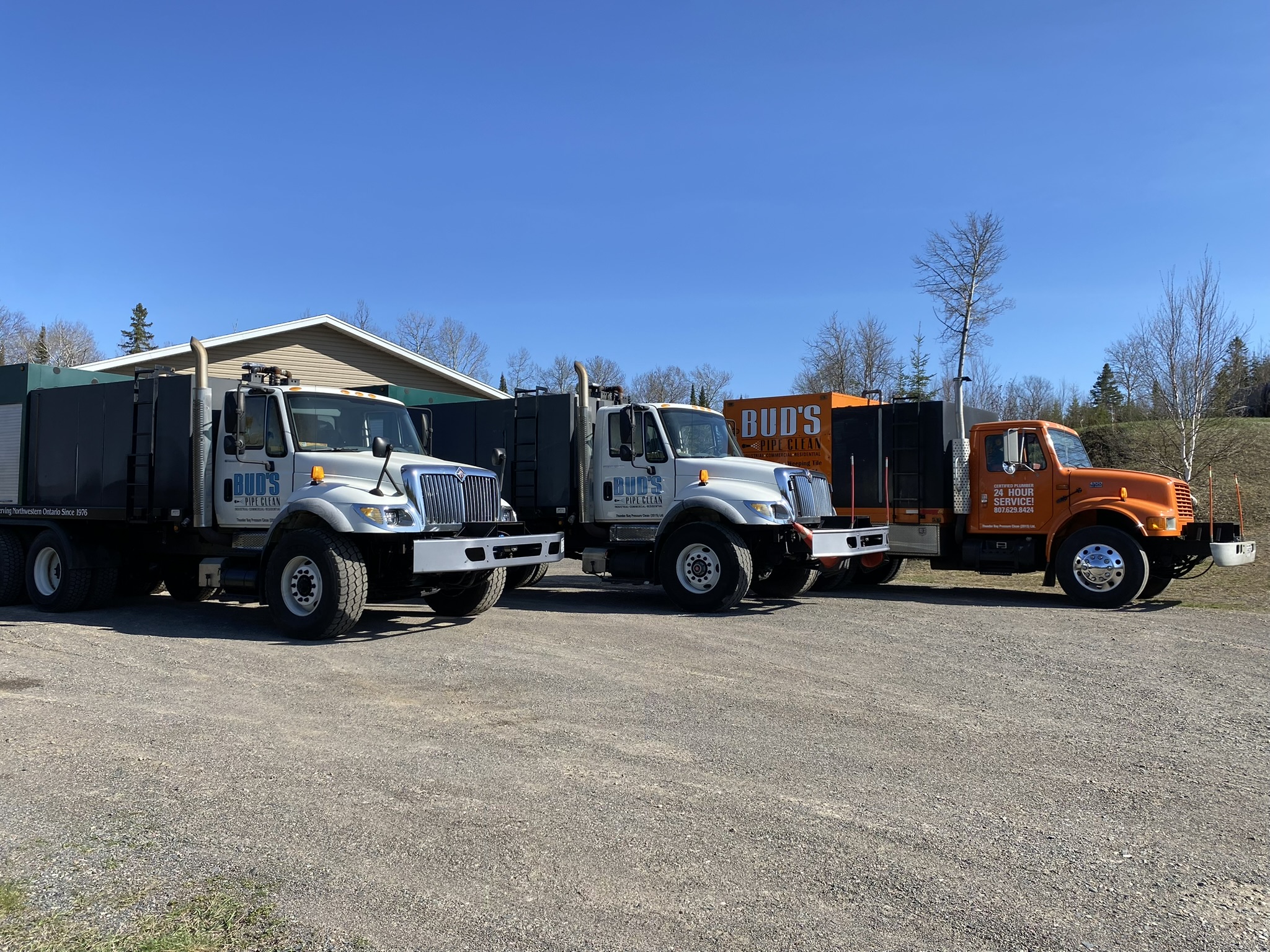 2 white and 1 orange cleaning trucks in front of a garage in the summer with Bud's Pipe Clean logo on the side and blue sky in the background