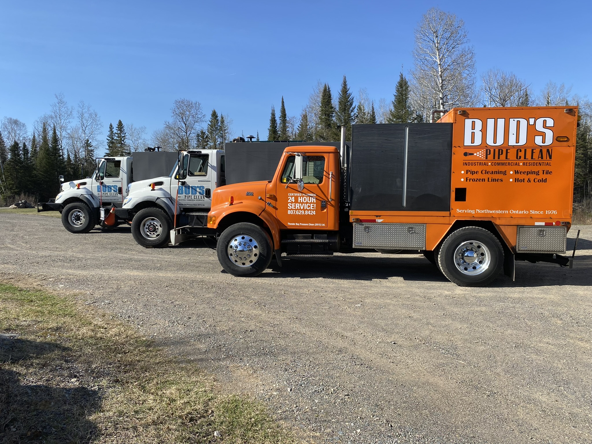 3 cleaning trucks in front of a garage in the summer with Bud's Pipe Clean logo on the side and blue sky in the background